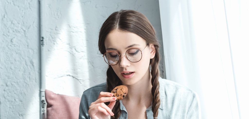 Woman with glasses on eating a weed cookie from online dispensary in Canada wccannabis. edibles canada. weed edibles. marijuana edibles canada.