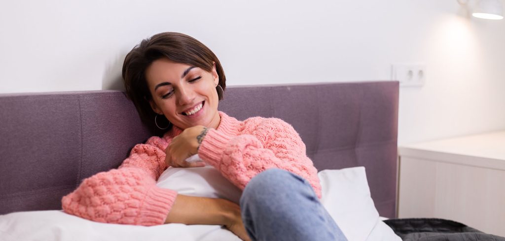 smiling and relaxed woman chilling in her bed at home after buying weed online at West Coast Cannabis online dispensary Canada.